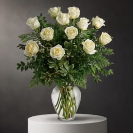 White roses arranged in a clear glass vase with mixed greenery