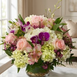 Pink roses and purple orchids arranged in a glass vase