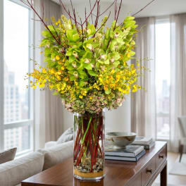 Tall vase arrangement with green orchids and yellow flowers