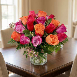 Bouquet of pink, orange, and red roses in a clear glass vase