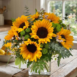Sunflower bouquet in a clear glass vase with mixed greenery