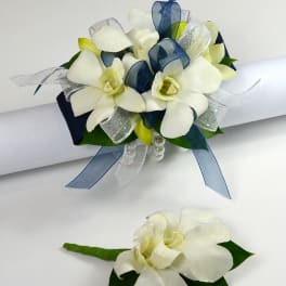 White floral wrist corsage with navy and silver ribbons and matching boutonniere.