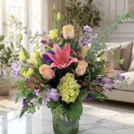Mixed bouquet with pink lilies, roses, and lavender flowers in a glass vase