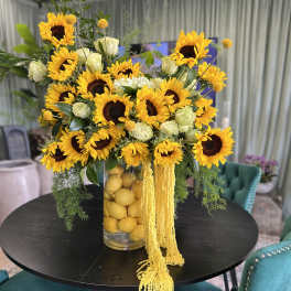 Sunflower arrangement in a clear vase with lemons and trailing yellow flowers