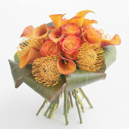 Orange roses and calla lilies with yellow pincushion blooms in a hand-tied bouquet