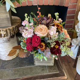 Mixed bouquet in a clear square vase with peach, red, and burgundy blooms