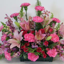 Fan-shaped arrangement of pink lilies, carnations, roses, and orchids in a green container