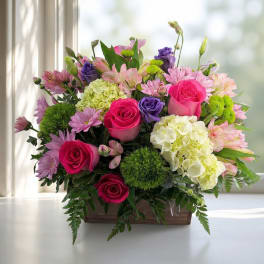 Mixed bouquet of pink and purple flowers in a low rectangular container