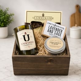Gift basket with candles, soap, and chocolates in a wooden crate