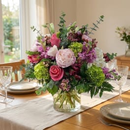 Pink and white mixed flower arrangement in a clear glass vase on a dining table
