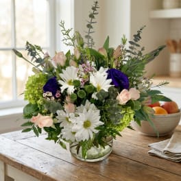 Mixed bouquet of white daisies, pale pink roses, and green blooms in a glass vase