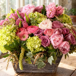 Pink and green floral arrangement in a rustic wooden container