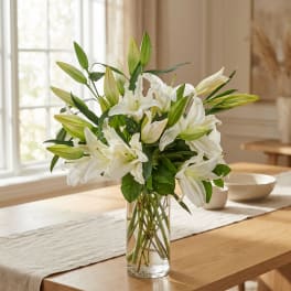 White lilies in a clear glass vase on a wooden table