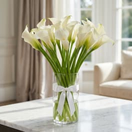 White calla lilies in a clear glass vase with a white ribbon