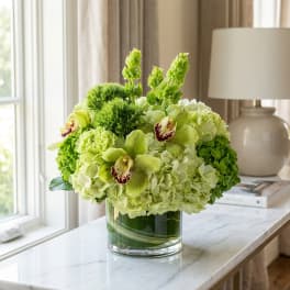 Green floral arrangement in a clear glass vase on a table