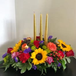 Floral centerpiece with three gold taper candles and bright mixed blooms