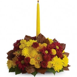 Yellow taper candle in a low arrangement of red and yellow flowers