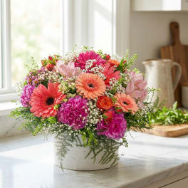 Mixed bouquet of pink, coral, and orange flowers in a white vase