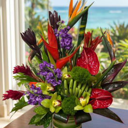 Tropical arrangement with red anthuriums, purple flowers, and bird of paradise in a striped vase.
