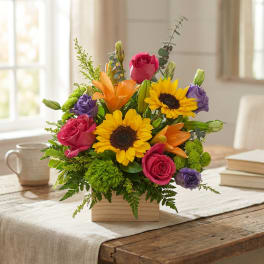 Mixed bouquet with sunflowers, roses, lilies, and purple blooms in a wooden box