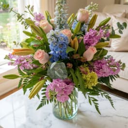 Mixed bouquet of pink roses, blue hydrangeas, and lilies in a glass vase