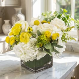 White and yellow flower arrangement in a square glass vase