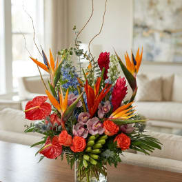 Tropical flower arrangement in a glass vase with orange bird-of-paradise and red blooms