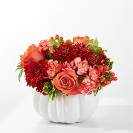 Orange and red floral arrangement in a white pumpkin vase