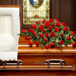 Red rose casket spray on a wooden coffin beside a white-lined interior