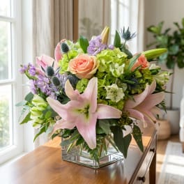 Mixed bouquet with pink lilies, peach roses, and green hydrangeas in a glass vase