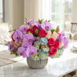 Bouquet of purple orchids, pink roses, and blue hydrangeas in a gray vase