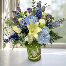 Blue and purple mixed bouquet with lilies and roses in a glass vase