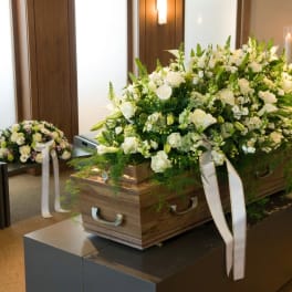 White floral casket spray on a wooden casket with a matching smaller arrangement nearby.