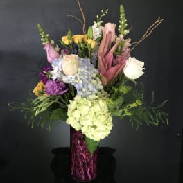 Tall mixed bouquet in a purple vase with roses, hydrangeas, and lilies