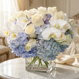 White roses and orchids with pale blue hydrangeas in a glass vase