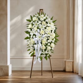 White floral standing wreath on an easel with a ribbon bow
