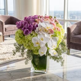 Purple and pink roses with white orchids in a glass vase