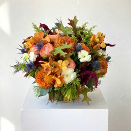 Autumn bouquet with orange, white, and burgundy flowers in a low container