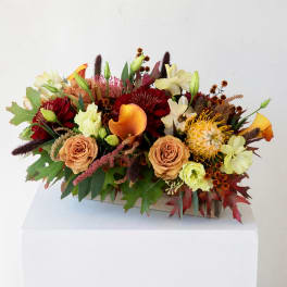 Autumn floral arrangement with orange calla lilies and red blooms in a wooden container