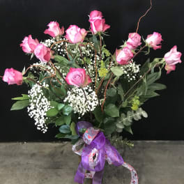 Pink roses arranged in a vase with baby's breath and ribbon