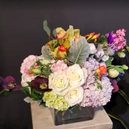 Mixed bouquet of roses, hydrangeas, and orchids in a square glass vase