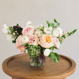 Mixed pastel flower arrangement in a glass vase on a wooden table