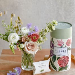 Flower arrangement in a glass vase beside a puzzle tin and caramel box