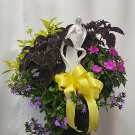 Potted mixed flowering plant arrangement with a white figurine and yellow ribbon