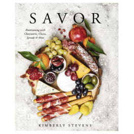Charcuterie board with fruit, cheese, olives, and breadsticks on a book cover
