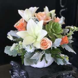 Peach roses and white lilies in a white pumpkin container