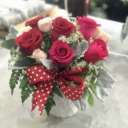 Bouquet of red and pink roses in a white vase with a red polka-dot ribbon