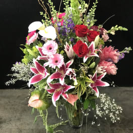 Large mixed bouquet with pink lilies, red roses, and white calla lilies in a glass vase