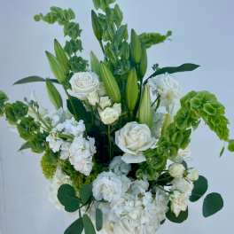 White roses and lilies arranged with green flowers in a glass vase