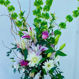 Tall floral arrangement with lilies, roses, and white daisies in a decorative vase
